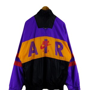 Puede incluir: Una chaqueta cortavientos de color morado, negro y naranja con la palabra "AIR" en letras grandes en la espalda. El logotipo de Nike swoosh est&aacute; por encima de la palabra "AIR" con la palabra "AIR" escrita debajo del swoosh.