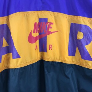 Puede incluir: Una chaqueta cortavientos amarilla, morada y verde con la palabra "AIR" en letras moradas y un logotipo Nike swoosh en rojo. La palabra "NIKE" est&aacute; escrita en letras blancas sobre el swoosh.