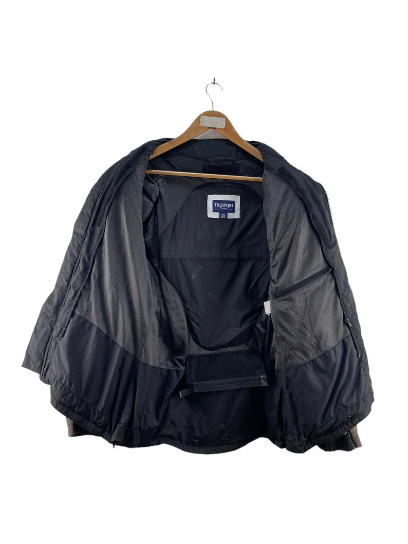 Puede incluir: Chaqueta negra con cierre de cremallera y etiqueta de la marca Triumph. La chaqueta tiene un forro de malla y dos bolsillos en el interior.