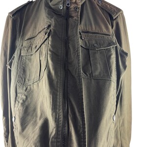 May include: Olive green bomber jacket with a zip-up front, multiple pockets, and a ribbed collar and cuffs. The jacket has a military-inspired design with shoulder epaulets and a relaxed fit. The fabric appears to be a durable, woven material.
