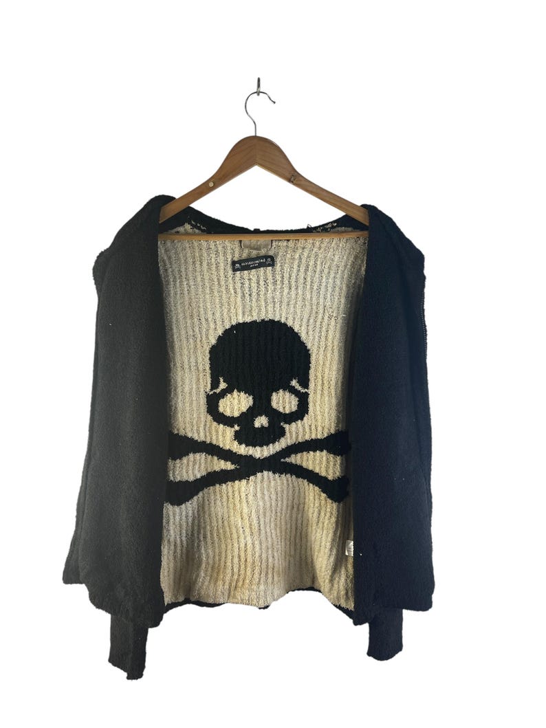 May include: Black open-front sweater with a large skull and crossbones design on the front. The sweater is hanging on a wooden hanger against a white background. The skull and crossbones are black.