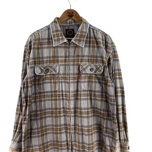 May include: A brown and blue plaid flannel shirt with a zipper closure. The shirt has two flap pockets on the chest and a red logo on the left side.