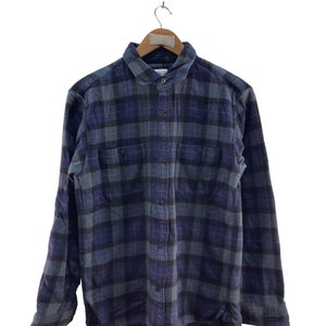Puede incluir: Una camisa de franela a cuadros azul y gris con mangas largas y cierre de botones.