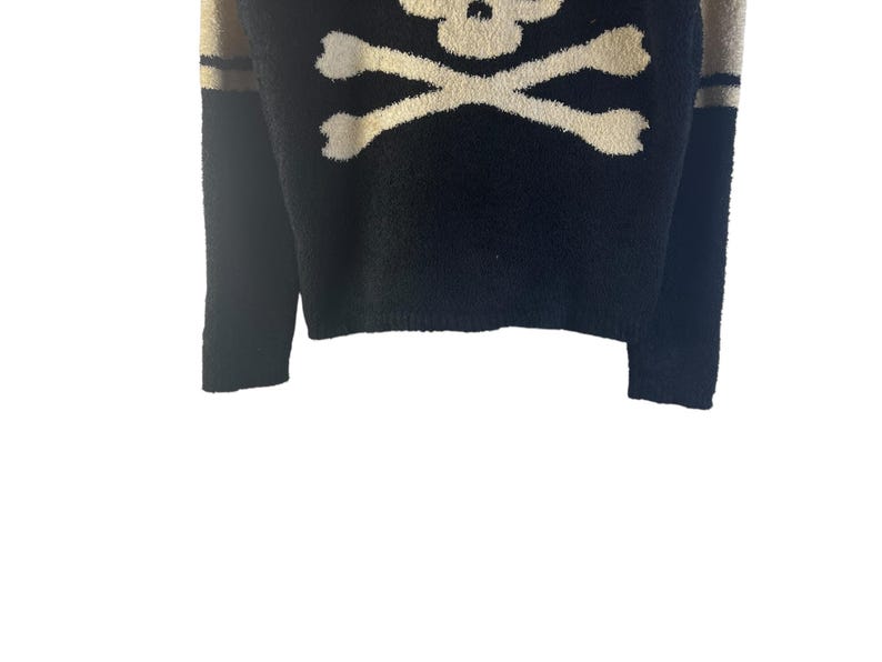 May include: Black sweater with a cream-colored skull and crossbones design. The sleeves have tan stripes near the shoulder. The sweater is a crew neck style.