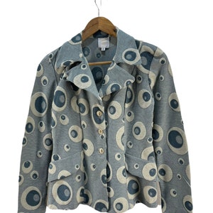 Puede incluir: Una chaqueta azul claro con un patrón de ojo blanco y azul. La chaqueta tiene cuello, mangas largas y cierre de botones.