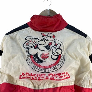 Puede incluir: Una chaqueta vintage blanca, roja y negra con un personaje de dibujos animados sosteniendo una pizza y el texto "Aoki's Pizza" y "Eat it before it gets cold!"