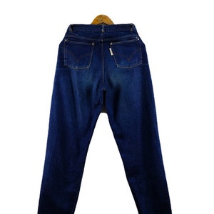 以下が含まれることがあります： ハイウエストでストレートレッグのダークブルーのデニムジーンズ。ジーンズは、クラシックな5ポケットのデザインとボタンフライです。