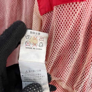 Puede incluir: Una etiqueta blanca con texto negro y s&iacute;mbolos, unida a una chaqueta roja y blanca. La etiqueta dice "取扱注意" (que significa "Precauciones de manejo") y "MADE IN CHINA". La etiqueta tambi&eacute;n incluye una serie de s&iacute;mbolos que indican las instrucciones de cuidado, como "30", "手洗い", "アイロン禁止" y "ドライクリーニング禁止".