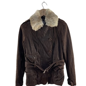 Puede incluir: Una chaqueta de cuero marrón con cuello de piel sintética y cinturón. La chaqueta tiene cierre de cremallera y detalles de botones.