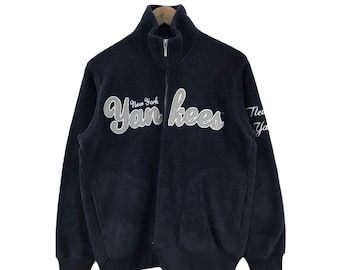May include: A navy blue fleece zip-up jacket with a white "New York Yankees" logo on the front. The jacket has a high collar and two pockets.