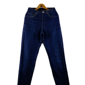 以下が含まれることがあります： 木製のハンガーにかけられた、濃い青色のデニムのジーンズ。ジーンズは、クラシックなストレートレッグスタイルで、ハイウエストです。