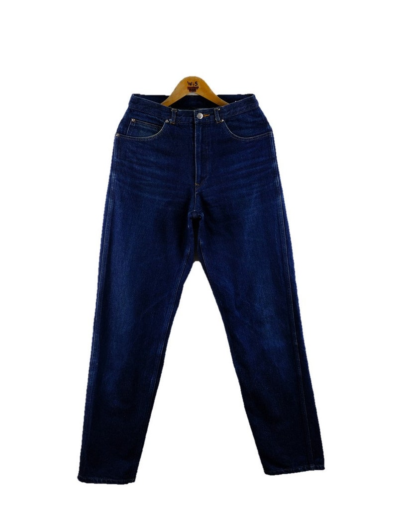 以下が含まれることがあります： 木製のハンガーにかけられた、濃い青色のデニムのジーンズ。ジーンズは、クラシックなストレートレッグスタイルで、ハイウエストです。