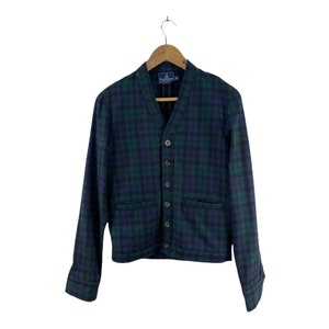 Pode incluir: Um cardigan xadrez azul e verde com decote em V e fecho de botões. O cardigan tem dois bolsos na frente e uma etiqueta que diz "Pendleton".