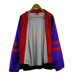 Puede incluir: Una chaqueta cortavientos de color morado y rojo con una cremallera negra y un forro blanco. La chaqueta tiene rayas rojas y blancas en las mangas.