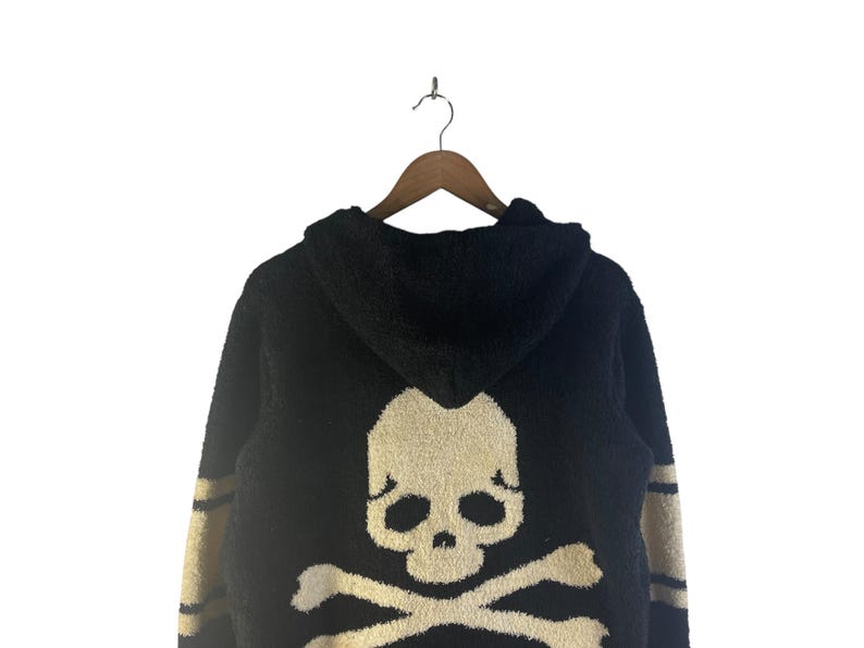 May include: Black hooded sweater with a large skull and crossbones design on the back. The skull is off-white, and the sweater has tan stripes on the sleeves.