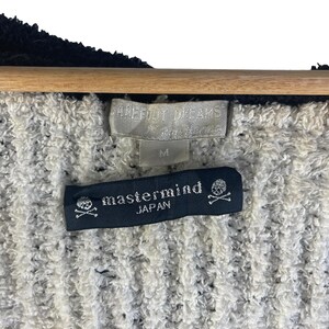 May include: Close-up of a textured, off-white and black fabric. The image shows two tags: one with the brand "Barefoot Dreams" and size "M", and another black tag with the text "mastermind JAPAN" and a skull and crossbones logo.