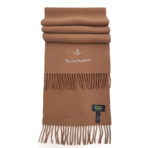 May include: A brown wool scarf with fringe. The scarf has the Vivienne Westwood logo embroidered on it in white. The scarf also has a black tag with the Vivienne Westwood logo.