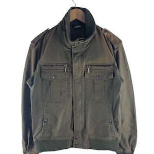 May include: Olive green bomber jacket with a high collar and multiple pockets. The jacket features a ribbed hem and cuffs, and a zipper closure. The jacket is hanging on a wooden hanger against a white background.