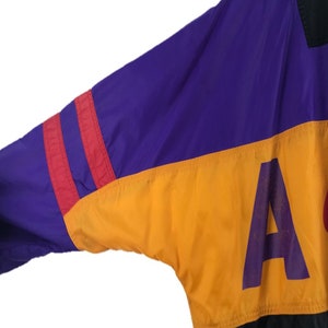 Puede incluir: Una chaqueta de color bloque en morado, rojo, amarillo y negro con una gran letra "A" morada en la secci&oacute;n amarilla.