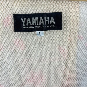 Puede incluir: Una etiqueta en blanco y negro con el texto "YAMAHA" y "YAMAHA MOTOR CO., LTD." en blanco. La etiqueta tambi&eacute;n tiene una etiqueta de tama&ntilde;o "L" blanca.
