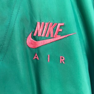 Puede incluir: Una chaqueta verde y morada con un logotipo de Nike Air rosa bordado en la parte delantera.