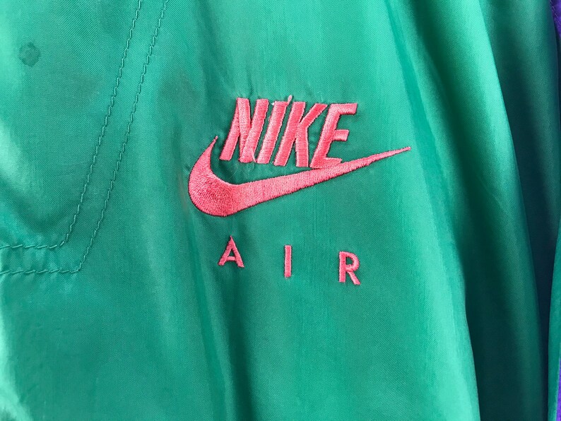 Puede incluir: Una chaqueta verde y morada con un logotipo de Nike Air rosa bordado en la parte delantera.