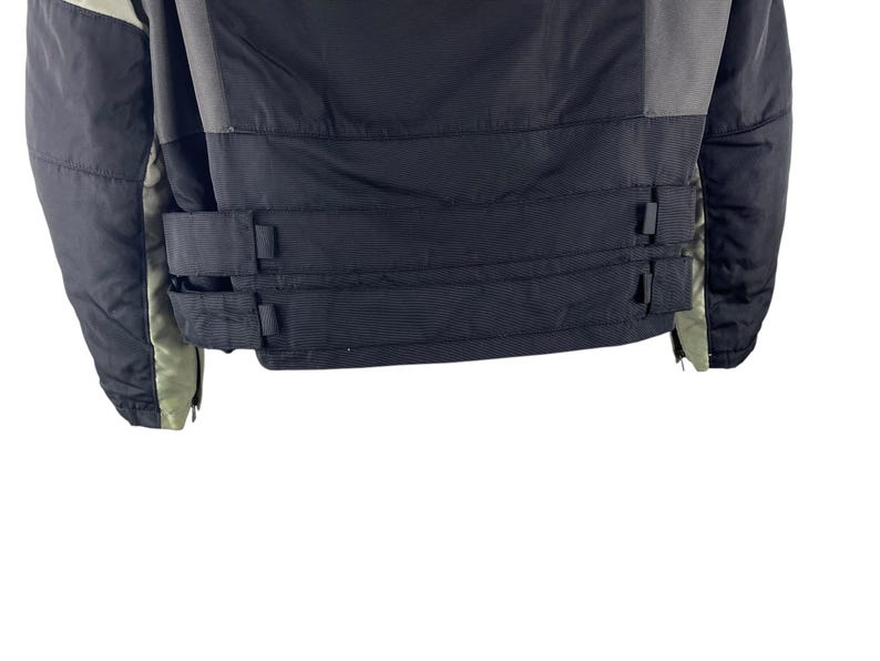 K&ouml;nnte beinhalten: Eine schwarze und graue Winterjacke mit hohem Kragen und Rei&szlig;verschluss. Die Jacke hat zwei schwarze Riemen mit Schnallen am unteren R&uuml;cken. Die &Auml;rmel sind schwarz und grau mit gr&uuml;nem Futter.