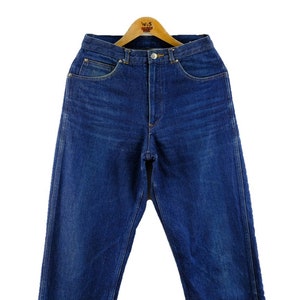 以下が含まれることがあります： クラシックなストレートレッグフィットのダークブルーデニムジーンズ。ジーンズはハイウエストでボタンフライです。