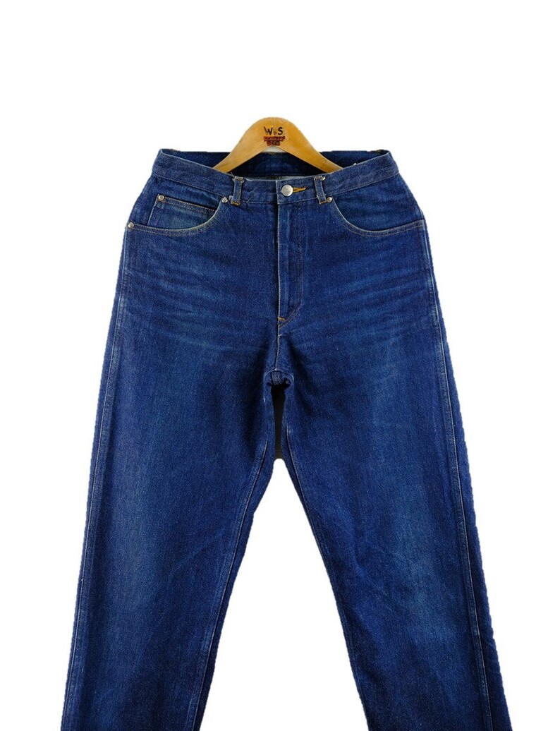 以下が含まれることがあります： クラシックなストレートレッグフィットのダークブルーデニムジーンズ。ジーンズはハイウエストでボタンフライです。