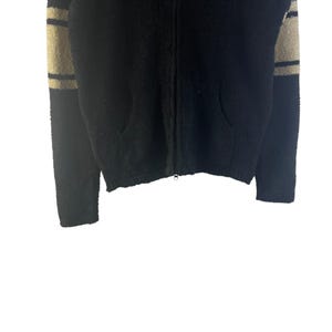 May include: Black zip-up sweater with beige and black striped sleeves. The sweater has two front pockets and a full zipper closure. The fabric appears to be a soft, textured material.