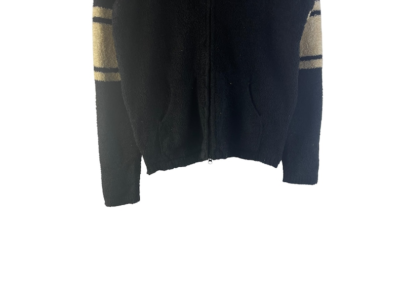 May include: Black zip-up sweater with beige and black striped sleeves. The sweater has two front pockets and a full zipper closure. The fabric appears to be a soft, textured material.