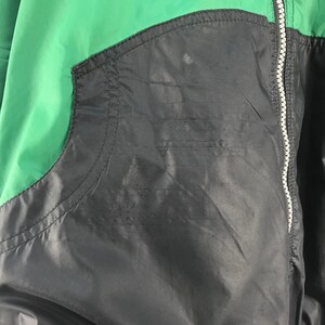 Puede incluir: Una chaqueta negra, verde y morada con cierre de cremallera. La chaqueta tiene un bolsillo en el lado izquierdo.