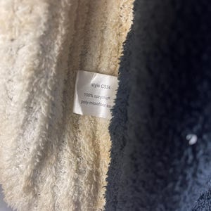 May include: Close-up of a soft, textured fabric in cream and navy blue. A small tag displays the text "style C534", "100% cozychic", and "poly-microfiber knit". The fabric appears to be part of a blanket or garment.