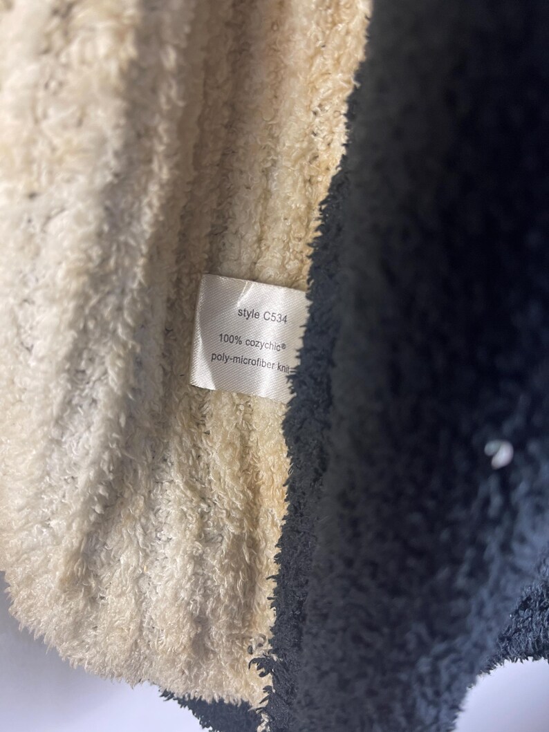 May include: Close-up of a soft, textured fabric in cream and navy blue. A small tag displays the text "style C534", "100% cozychic", and "poly-microfiber knit". The fabric appears to be part of a blanket or garment.