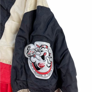 Puede incluir: Chaqueta negra y roja con una raya blanca y negra. La chaqueta tiene un parche grande en la manga izquierda con un personaje de dibujos animados sosteniendo una pizza y el texto "Roteli's Pizza" y "Eat it before it gets cold".