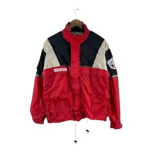 Puede incluir: Una chaqueta cortavientos roja, negra y blanca con cierre de cremallera y capucha con cord&oacute;n. La chaqueta tiene un parche de logotipo en la manga izquierda que dice "Rocky's Pena".