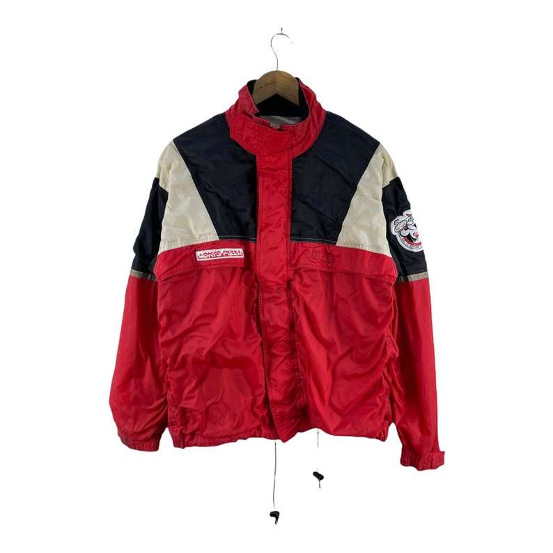 Puede incluir: Una chaqueta cortavientos roja, negra y blanca con cierre de cremallera y capucha con cord&oacute;n. La chaqueta tiene un parche de logotipo en la manga izquierda que dice "Rocky's Pena".