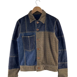 Puede incluir: Una chaqueta vaquera azul y marrón con un patrón de espiga en el lado derecho. La chaqueta tiene cierre de botones y un bolsillo de parche en el lado izquierdo.