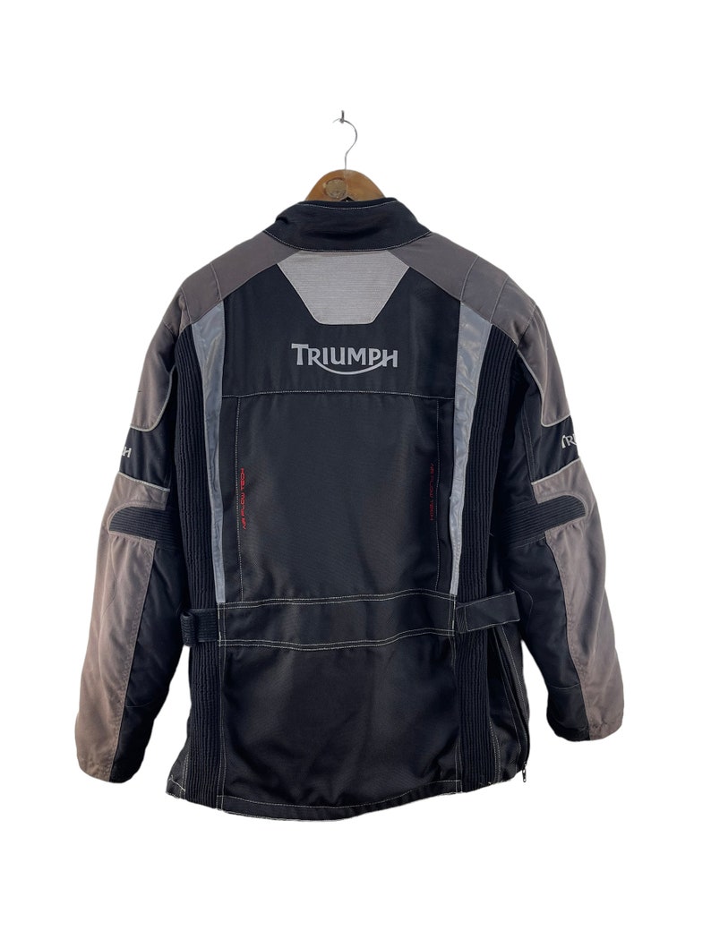 Puede incluir: Chaqueta de moto negra y gris con la palabra "TRIUMPH" en letras blancas en la espalda.