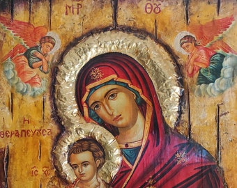 May include: A traditional religious icon depicting the Virgin Mary holding the baby Jesus. The icon is painted on a wooden panel with gold leaf accents and features a red and gold color scheme. The text "Η θεραπευτρια" is written in Greek on the icon.