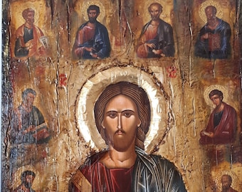 Op de afbeelding: Een religieus icoon schilderij in vintage stijl, dat Jezus Christus afbeeldt met een open boek met Griekse tekst. Het schilderij is ingelijst in een houten lijst met een verweerde afwerking. De achtergrond is van een textuurrijke gouden kleur. Het schilderij is omringd door kleinere iconen van andere figuren.