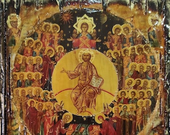 Puede incluir: Una pintura de icono religioso de estilo vintage que representa a Jesucristo rodeado de un círculo de santos y ángeles. La pintura está sobre un panel de madera con un aspecto desgastado y envejecido. El fondo es azul oscuro con estrellas doradas.