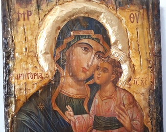 Op de afbeelding: Een traditioneel Byzantijns icoon dat de Maagd Maria afbeeldt die het kindje Jezus vasthoudt. Het icoon is geschilderd op een houten paneel met accenten van bladgoud. De achtergrond is een getextureerde houtnerf. Het icoon is gesigneerd met "Vanas Collection".
