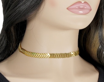 May include: A gold choker necklace with a chain made of small, overlapping, arrow-shaped links.