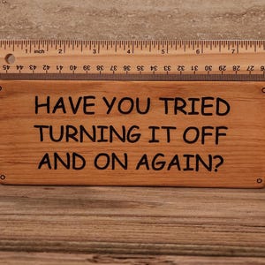 May include: A wooden sign with the text "Have you tried turning it off and on again?" in black lettering.