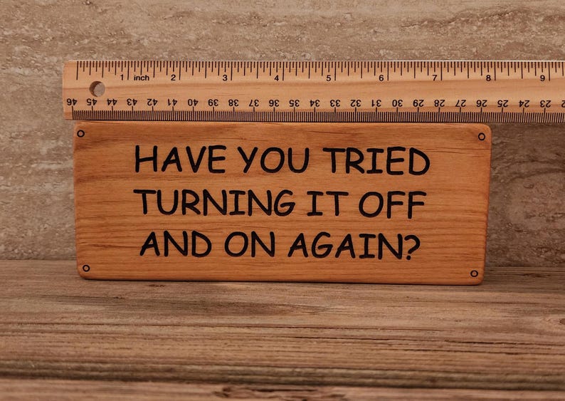 May include: A wooden sign with the text "Have you tried turning it off and on again?" in black lettering.