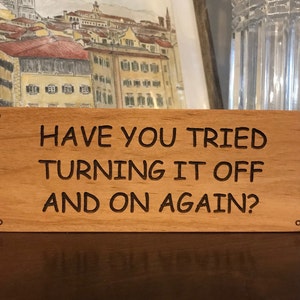 May include: A wooden sign with the text "Have you tried turning it off and on again?" in black lettering.