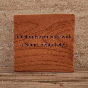 Op de afbeelding: Een houten onderzetter met een natuurlijke houtnerf. De onderzetter heeft de tekst "Customize on back with a Name, School etc..." gegraveerd op de voorkant.