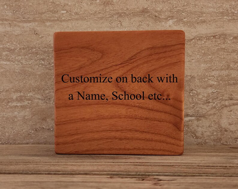 Op de afbeelding: Een houten onderzetter met een natuurlijke houtnerf. De onderzetter heeft de tekst "Customize on back with a Name, School etc..." gegraveerd op de voorkant.