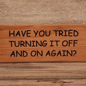 May include: A wooden sign with the text "Have you tried turning it off and on again?" in black lettering.